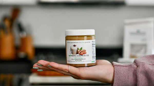 Hand holding a jar of Rawmantic raw creamy almond butter in a kitchen