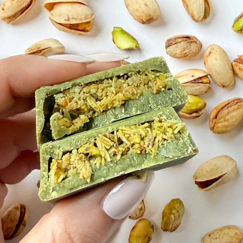 Hand holding a matcha Dubai chocolate bar split open to show the pistachio knafeh filling