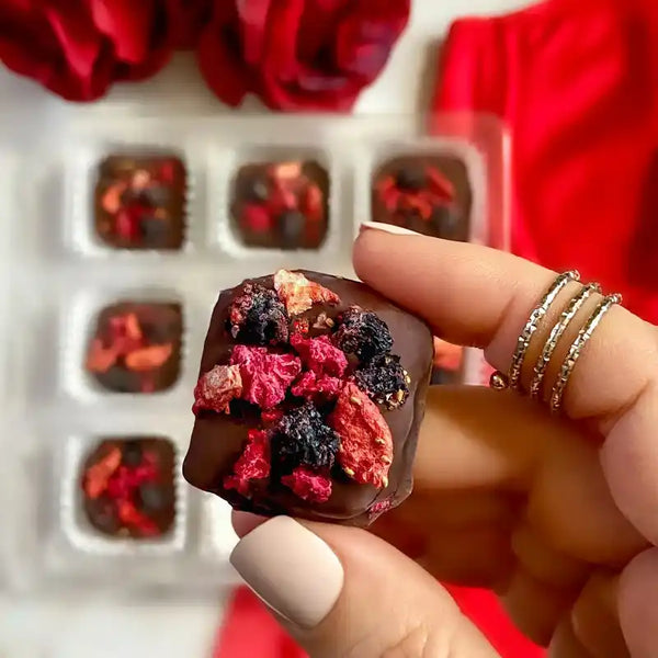 Hand holding a mixed berry chocolate truffle from a box of 12